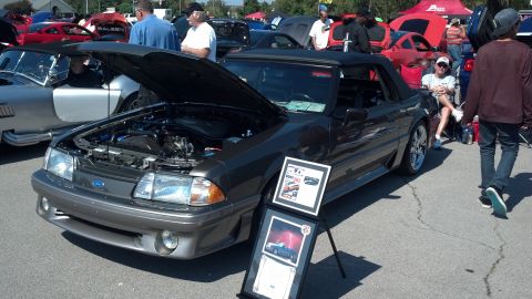 2007 Ford Mustang - A dark gray 1993 Ford Mustang convertible is displayed with its hood open, alongside other vehicles and attendees at a car show.