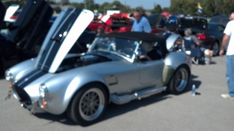 2007 Ford Mustang - A silver Shelby Cobra replica is displayed with its hood open at an outdoor car show.