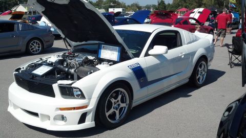 2007 Ford Mustang - A white Ford Mustang is displayed with its hood open at a car show, revealing the engine and a descriptive sign.
