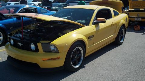2007 Ford Mustang - A yellow 2007 Ford Mustang is displayed with its hood open at a car show, revealing the engine compartment.