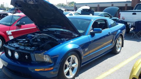 2007 Ford Mustang - A blue Ford Mustang GT is displayed with its hood open at an outdoor car show, alongside other vehicles.