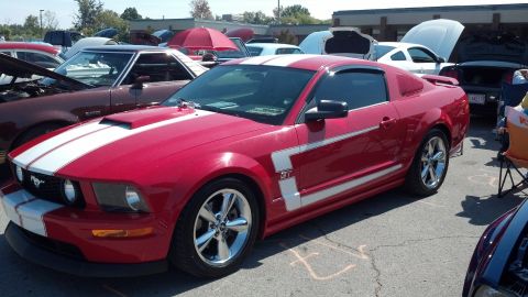 2007 Ford Mustang - A red 2007 Ford Mustang coupe with white racing stripes is displayed at a car show.