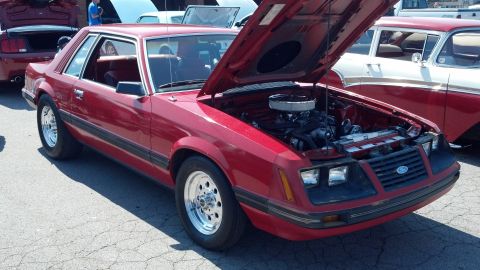 2007 Ford Mustang - Red coupe with hood open at a car show, parked next to other vehicles.