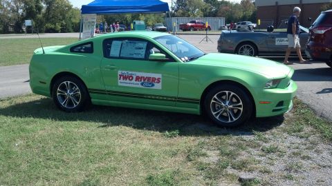2007 Ford Mustang - A bright green Ford Mustang is parked on grass next to a paved area with other vehicles.
