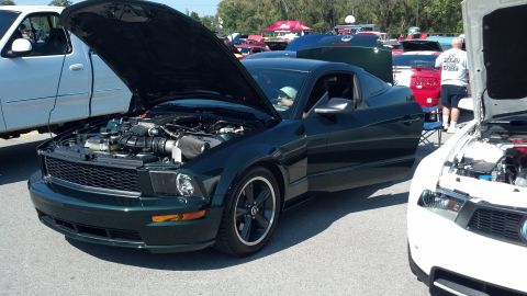 2007 Ford Mustang - A dark green coupe is displayed with its hood and door open at a car show.