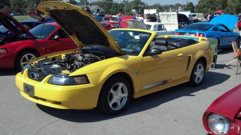 2007 Ford Mustang - A yellow convertible Mustang is displayed with its hood up at a car show, alongside other vehicles.