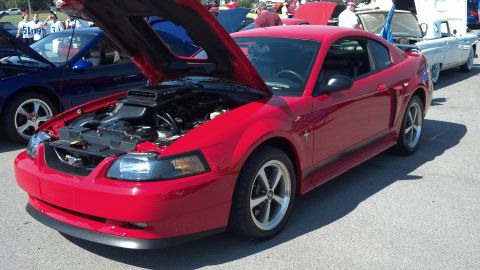 2007 Ford Mustang - Red Ford Mustang at a car show with its hood open, revealing the engine bay.