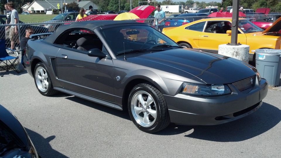 Dark gray convertible parked at an outdoor event. Yellow car in background