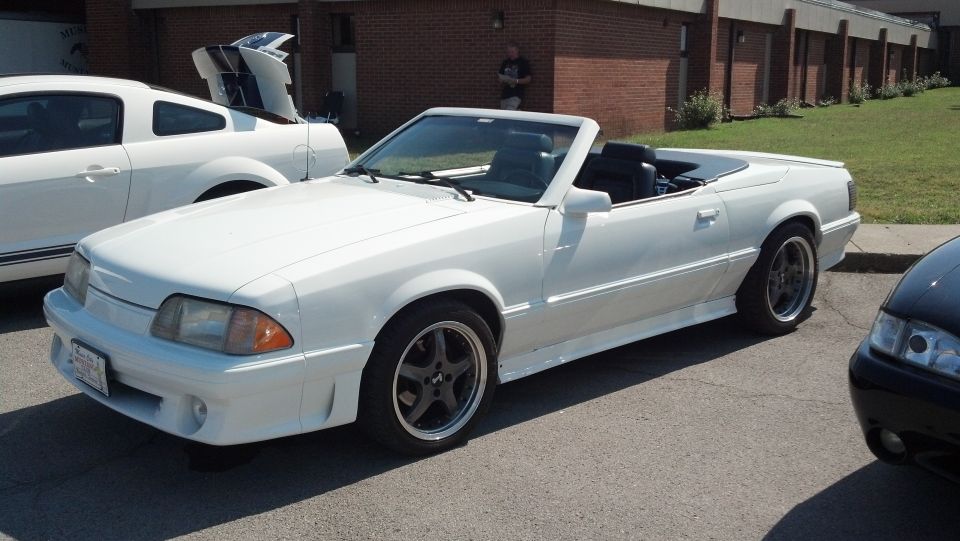White convertible with black interior parked next to a white coupe with its trunk open