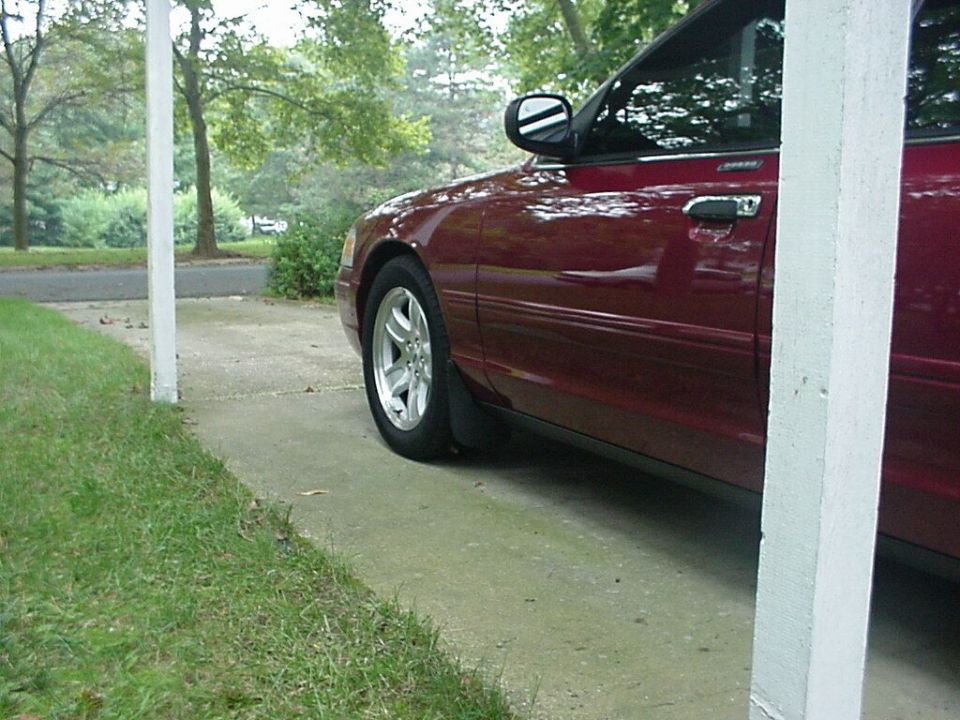 Dark red sedan's driver side showing front wheel, mud flap and door on a driveway.