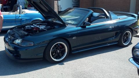 2007 Ford Mustang - A dark teal 1994 Ford Mustang convertible is displayed with its hood open, parked next to another Mustang at a car show.