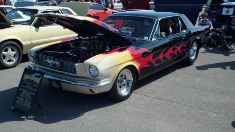 2007 Ford Mustang - A classic Ford Mustang with a flame paint job is displayed with its hood open at a car show.
