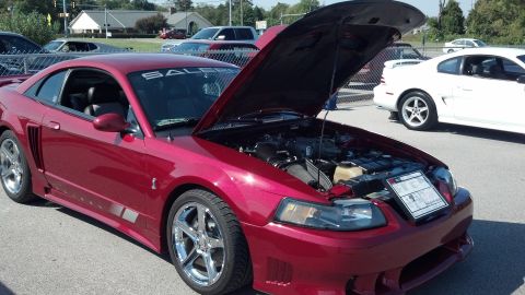 2007 Ford Mustang - A red 2007 Ford Mustang coupe is displayed with its hood open, revealing the engine and a placard detailing its features.