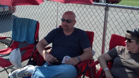 2007 Ford Mustang - Two people relax in lawn chairs at an outdoor event, with a fence and a car visible in the background.