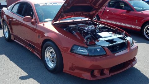 2007 Ford Mustang - A red 2007 Ford Mustang, identified as a Saleen model, is displayed with its hood open, revealing a supercharged engine. Another Mustang is…