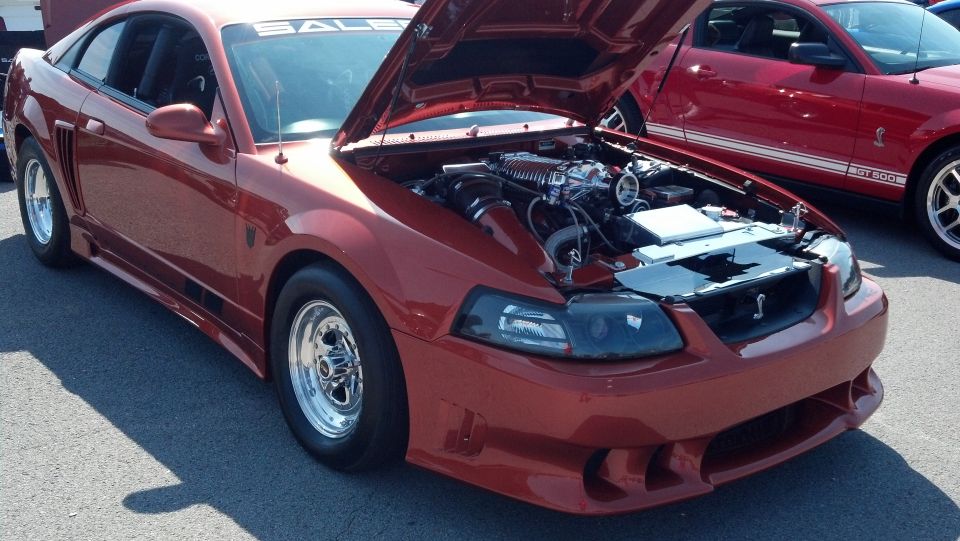 Red 2007 Ford Mustang with hood open, showing engine and supercharger. Drag racing tires visible