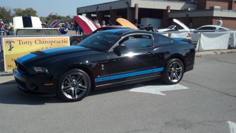 2007 Ford Mustang - A black 2007 Ford Mustang GT500 with blue racing stripes is displayed at an outdoor car show.