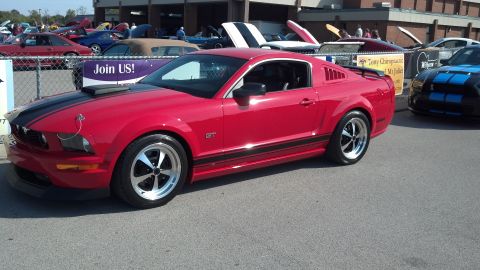 2007 Ford Mustang - A red 2007 Ford Mustang GT is parked at a car show with other vehicles visible in the background.