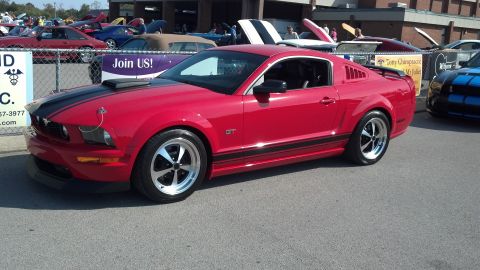 2007 Ford Mustang - A red 2007 Ford Mustang GT is parked at a car show, with other vehicles visible in the background.
