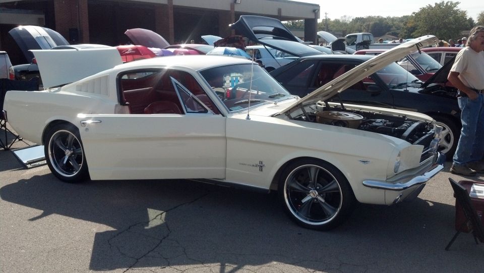 Cream-colored 1965 Ford Mustang coupe with red interior, hood and trunk open, custom wheels