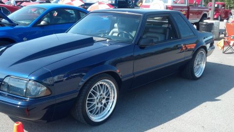 2007 Ford Mustang - A dark blue coupe, likely a 1990 Ford Mustang, is parked at a car show with an aftermarket hood and custom wheels.
