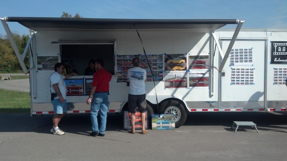 White trailer with display windows showing model cars, people standing nearby
