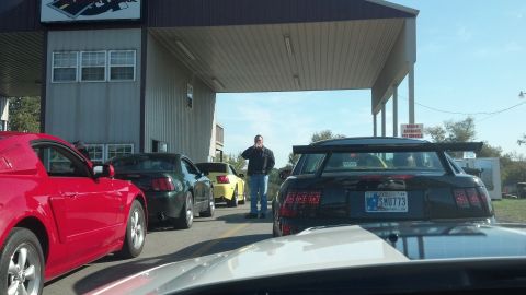 2007 Ford Mustang - Several Ford Mustangs are lined up at a registration booth, with a man standing in the middle.