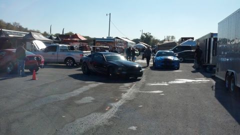 2007 Ford Mustang - Several vehicles, including a black 2007 Ford Mustang, are parked at an outdoor event with tents and trailers in the background.