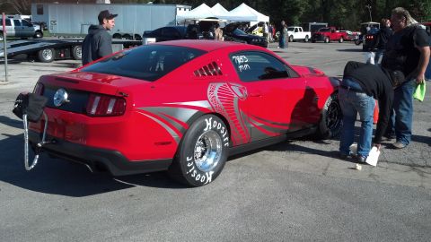 2007 Ford Mustang - A red Ford Mustang modified for drag racing is parked on asphalt with people around it.