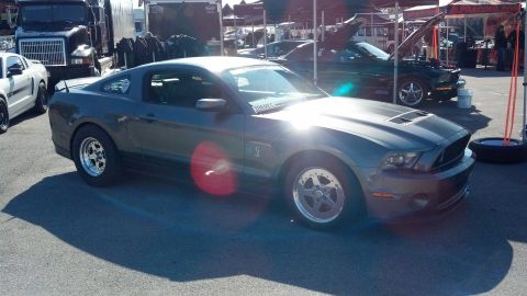 2007 Ford Mustang - A gray Ford Mustang is parked at an outdoor event, with a dark green Mustang and a large truck in the background.