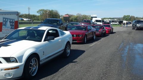 2007 Ford Mustang - Several Ford Mustangs are lined up on an asphalt surface under a clear sky, with a trailer visible to the left.