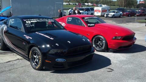 2007 Ford Mustang - Two Ford Mustangs, one black and one red, are parked at a drag racing event.