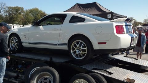 2007 Ford Mustang - A white Ford Mustang GT500 with blue racing stripes is being transported on a trailer.