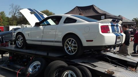 2007 Ford Mustang - White 2007 Ford Mustang with blue racing stripes is loaded onto a trailer.