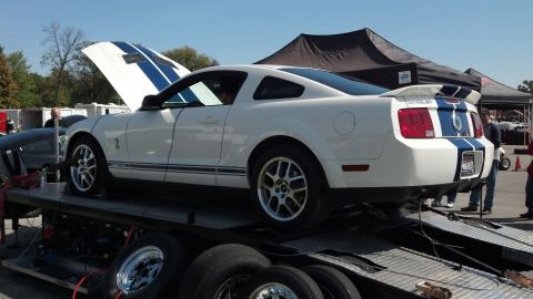 2007 Ford Mustang - A white Ford Mustang Shelby GT500 is loaded onto a trailer, its hood open, revealing blue racing stripes.