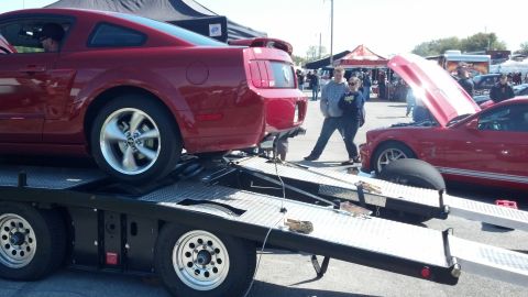 2007 Ford Mustang - Two red Ford Mustangs are visible at an outdoor event, one being loaded onto a car hauler.