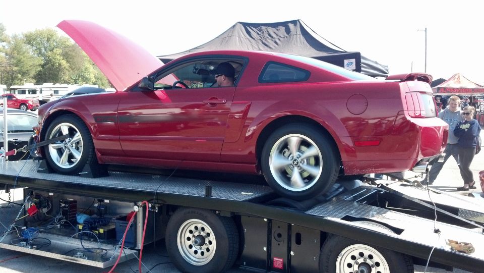 Red Ford Mustang on a dynamometer, hood open, side view