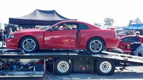 2007 Ford Mustang - A red Ford Mustang GT is loaded onto a car hauler, with another Mustang visible behind it at an outdoor event.
