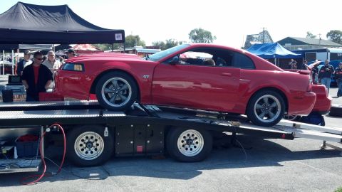 2007 Ford Mustang - A red Ford Mustang GT is loaded onto a car hauler, with other vehicles and tents in the background.