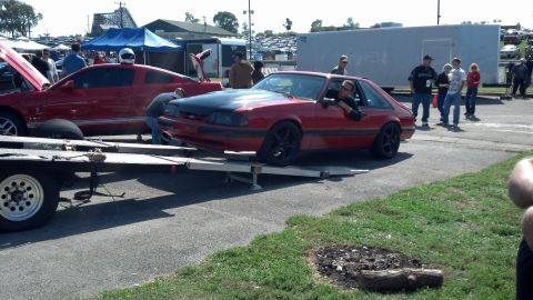 2007 Ford Mustang - A red coupe with a black hood is being loaded onto a trailer, with another red car visible in the background.