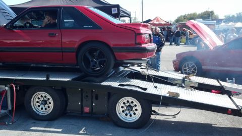 2007 Ford Mustang - A red coupe is loaded onto a trailer, with another red car visible in the background with its hood open.