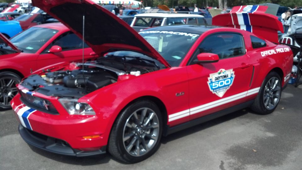 Red Ford Mustang with white racing stripes and Daytona 500 decals, hood open, rear spoiler