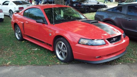 2007 Ford Mustang - A red 2007 Ford Mustang coupe is parked on grass, with other vehicles visible in the background.