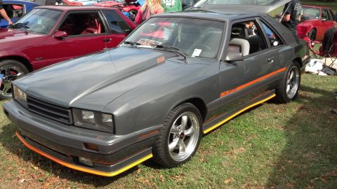 2007 Ford Mustang - Gray coupe with orange side stripe and yellow trim parked on grass next to a red coupe.