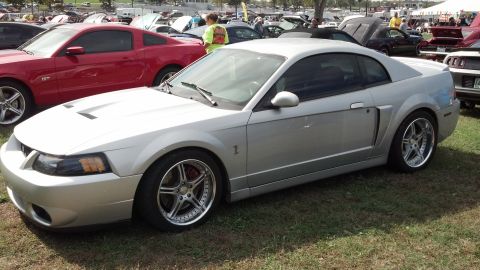 2007 Ford Mustang - A silver Ford Mustang coupe is parked on grass at an outdoor event with other vehicles visible.