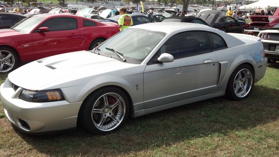 Silver Ford Mustang coupe with aftermarket wheels and red brake calipers, parked on grass