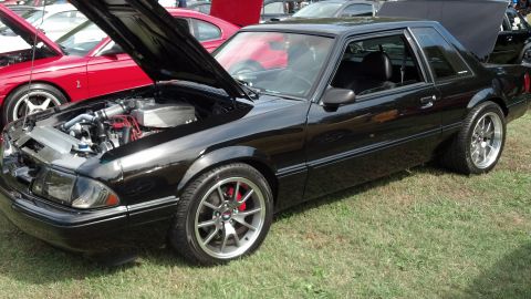 2007 Ford Mustang - A black 1987 Ford Mustang coupe is parked on grass with its hood open, revealing the engine bay. Another red Mustang is visible in the back…
