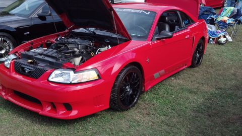 2007 Ford Mustang - A red Ford Mustang is parked on grass with its hood open, revealing the engine bay. Another car is visible to the left.