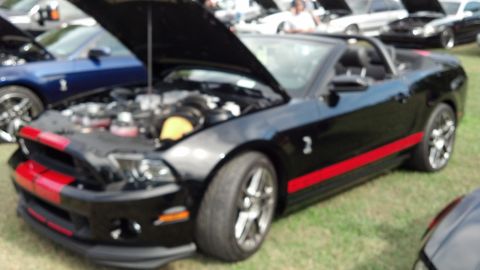 2007 Ford Mustang - A black convertible with red racing stripes is parked on grass with its hood open.
