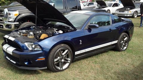 2007 Ford Mustang - A blue 2007 Ford Mustang GT500 is displayed with its hood open, revealing the engine, while other vehicles are parked nearby.